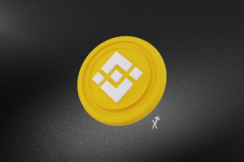 Pièce jaune frappée du logo Binance, inclinée sur un fond noir granuleux