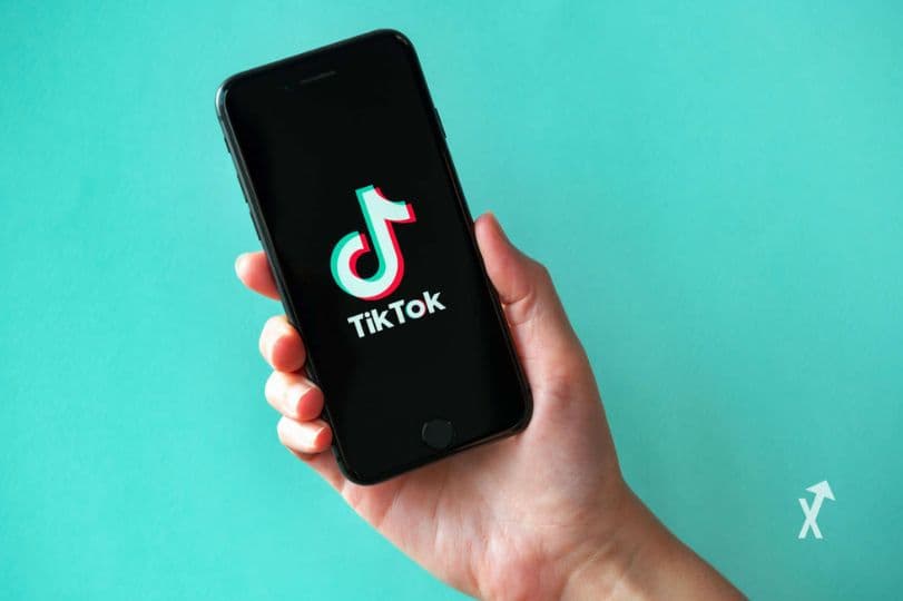 Main tenant un smartphone noir affichant le logo TikTok sur fond turquoise